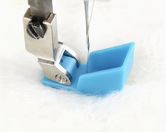 Könnte beinhalten: Nahaufnahme eines Nähmaschinenfußes mit einer blauen Kunststoffführung. Der Metallfuß ist mit einer Schraube an der Maschine befestigt. Eine Nadel mit Faden ist sichtbar, bereit zum Nähen. Der Hintergrund ist ein weicher, weißer Stoff.