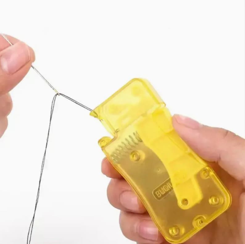 Puede incluir: Un enhebrador de agujas de pl&aacute;stico amarillo con una caja de pl&aacute;stico transparente. El enhebrador tiene una peque&ntilde;a cuchilla afilada y una ranura para enhebrar la aguja. La caja tiene la palabra "BUQI" impresa.