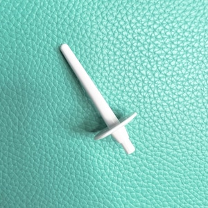May include: White plastic bobbin winder for a sewing machine. The winder is on a light blue textured surface.