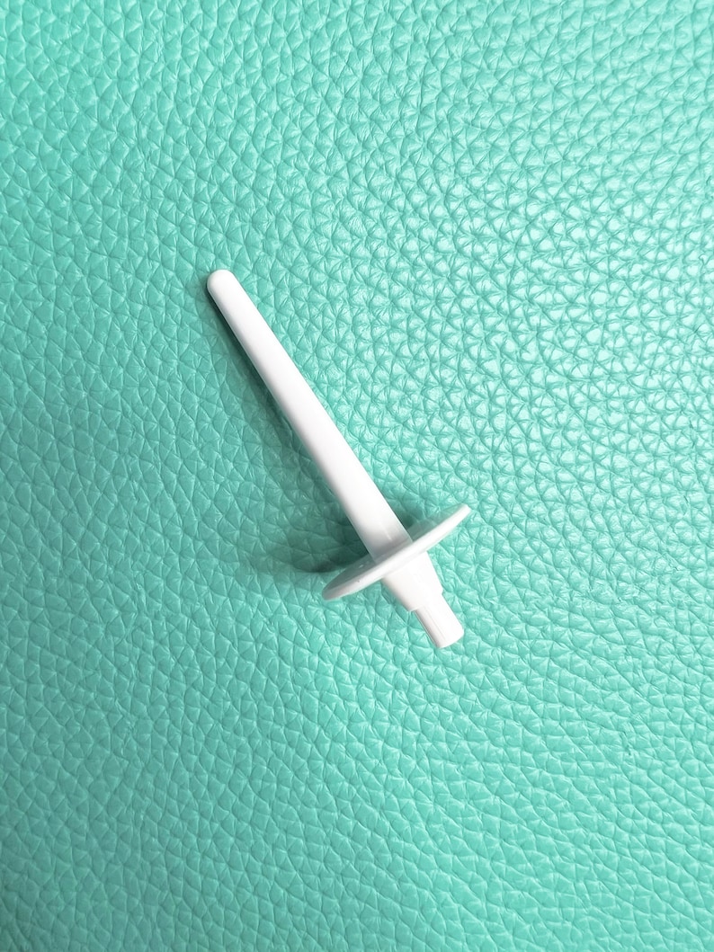 May include: White plastic bobbin winder for a sewing machine. The winder is on a light blue textured surface.