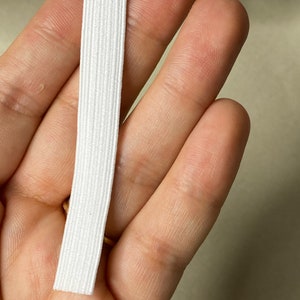 May include: White elastic band, approximately 1/2 inch wide, held in a hand.