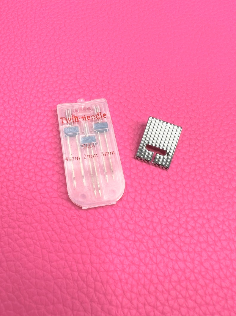 May include: A clear plastic case containing twin needles for sewing. The case has the text "Twin needle" and "Size 2mm 3mm" printed on it. The needles are silver and come in three different sizes. A silver metal sewing machine foot is also pictured.