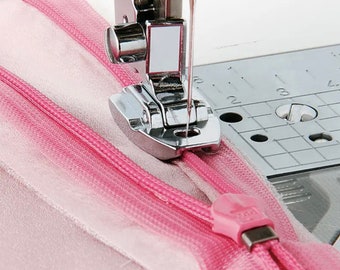 May include: Close-up of a sewing machine needle and foot sewing a pink zipper tape. The foot is designed for sewing zippers.