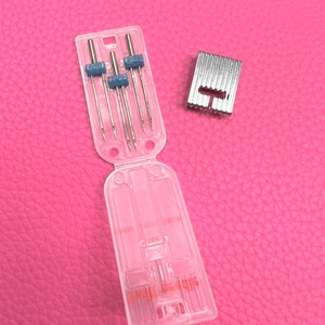 May include: A clear plastic case containing six sewing machine needles and a silver metal sewing machine foot. The case has the text "SIZE 11/70" printed on it.