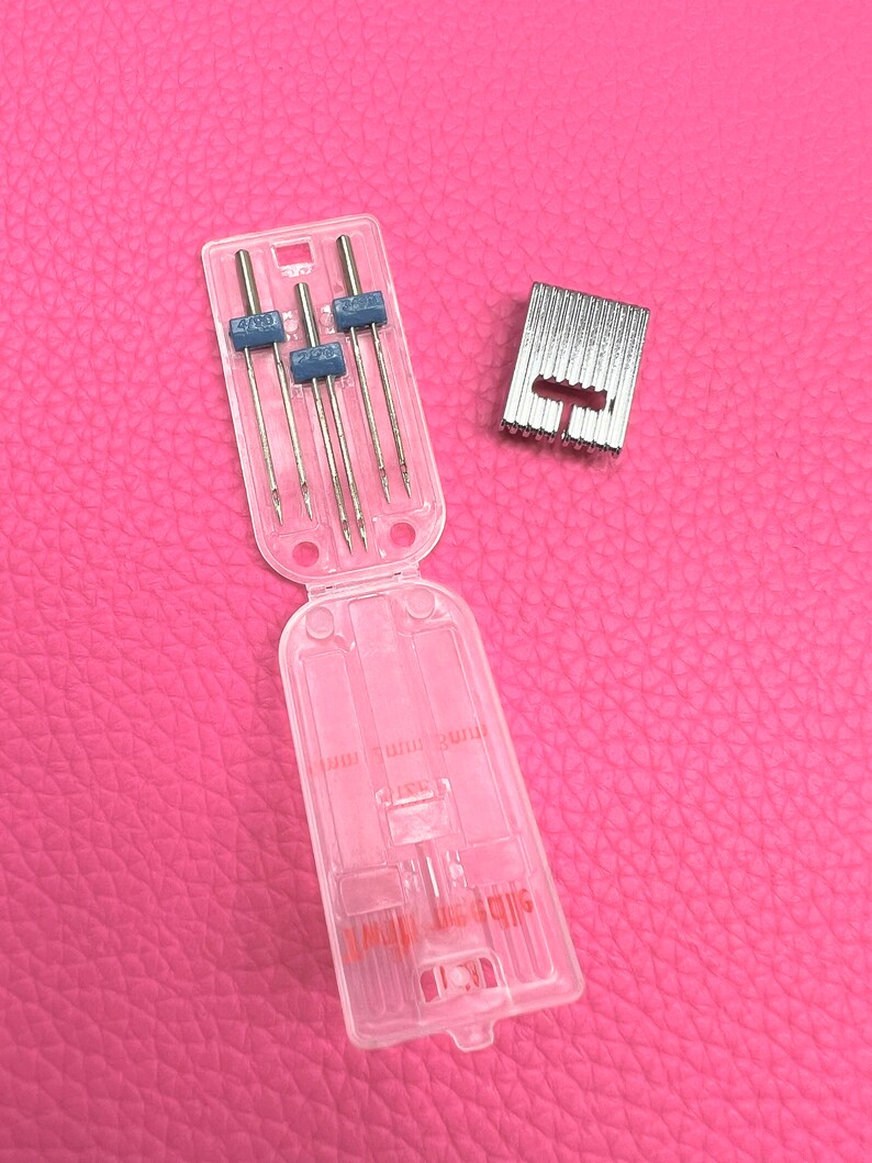 May include: A clear plastic case containing six sewing machine needles and a silver metal sewing machine foot. The case has the text "SIZE 11/70" printed on it.