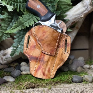 May include: A brown leather holster with a stitched design, holding a silver revolver with a wooden grip.