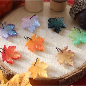 Può includere: Otto piccoli ciondoli a forma di foglia d'acero realizzati in resina traslucida in vari colori, tra cui rosso, arancione, giallo, verde, blu e viola. Ogni foglia presenta un piccolo anellino di metallo sulla parte superiore e una superficie ruvida.