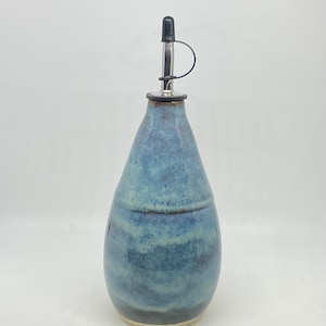 Puede incluir: Una botella de aceite de cerámica hecha a mano con un esmalte azul y gris. La botella tiene forma de lágrima y una boquilla de acero inoxidable con tapa negra. Accesorio de cocina decorativo.