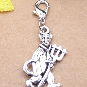 Könnte beinhalten: Ein silberfarbener Charm-Anhänger, der einen Teufel mit einem Dreizack darstellt. Der Anhänger ist an einem silberfarbenen Karabinerverschluss befestigt. Der Teufel hat Hörner und einen Schwanz. Der Charm ist für ein Armband oder eine Halskette.