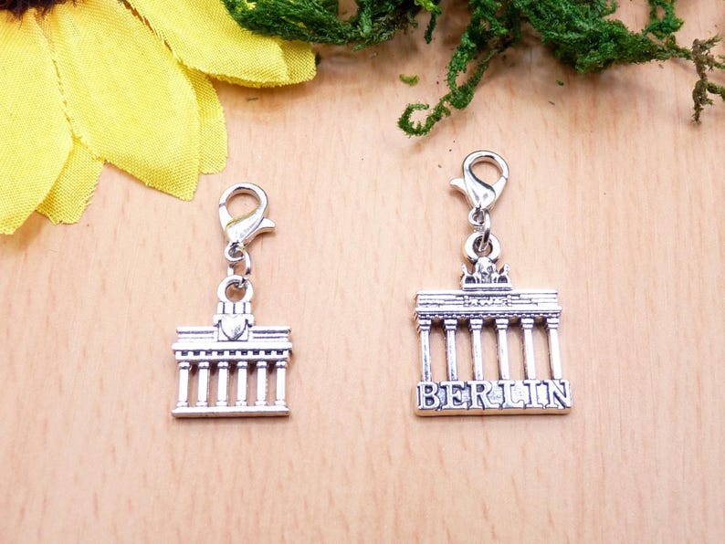K&ouml;nnte beinhalten: Zwei silberfarbene Berlin Brandenburger Tor Charms mit Karabinerhaken. Ein Charm hat das Wort "BERLIN" eingraviert. Die Charms sind detailliert mit S&auml;ulen und architektonischen Merkmalen, ideal f&uuml;r Schmuckherstellung oder als Souvenir.