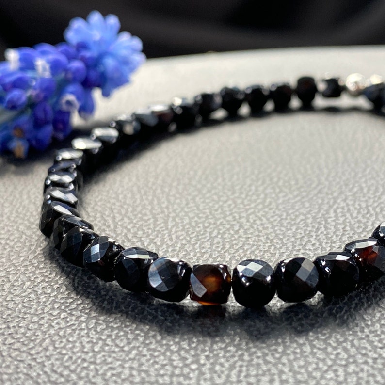 May include: A black gemstone bracelet with faceted beads. The bracelet is made with black onyx and a single brown gemstone.