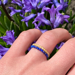 May include: A delicate ring made of two rows of small beads. The top row is made of light yellow beads, and the bottom row is made of dark blue beads.