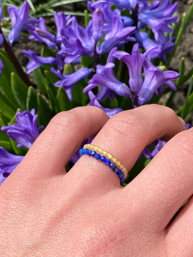 May include: A delicate ring made of two rows of small beads. The top row is made of light yellow beads, and the bottom row is made of dark blue beads.