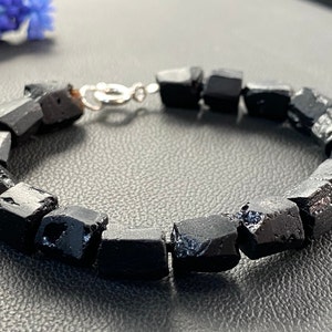 May include: A black gemstone bracelet with a silver clasp. The bracelet is made of rough, faceted black stones.