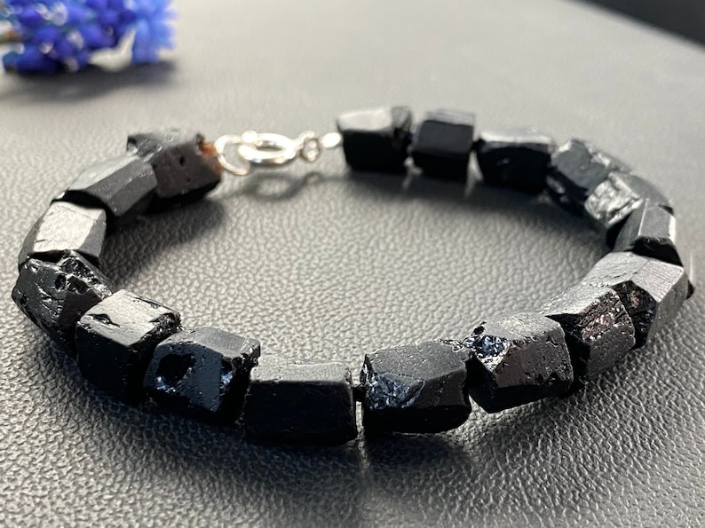 May include: A black gemstone bracelet with a silver clasp. The bracelet is made of rough, faceted black stones.