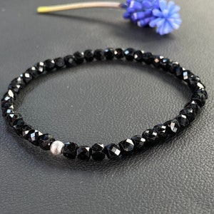 May include: A black beaded bracelet with a single silver bead. The bracelet is made of faceted black beads and is approximately 7 inches in length.