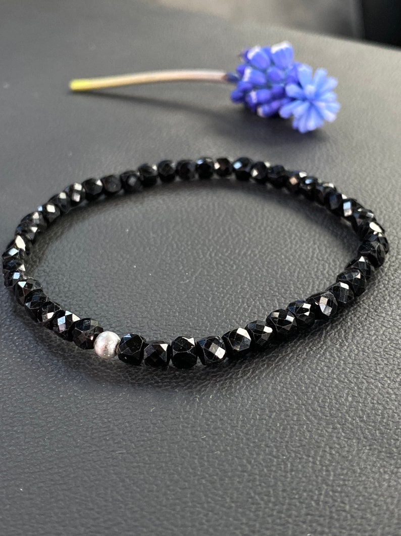 May include: A black beaded bracelet with a single silver bead. The bracelet is made of faceted black beads and is approximately 7 inches in length.