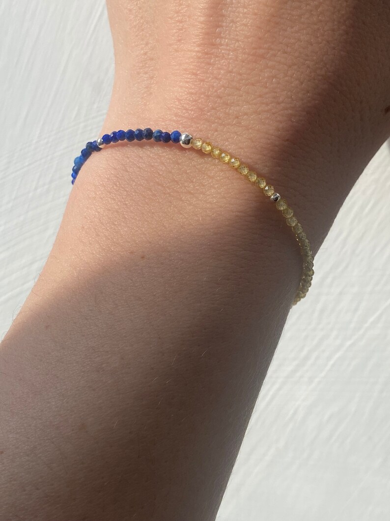 May include: A blue and yellow beaded bracelet with silver accents. The bracelet is made of small, round beads and is strung on a thin, silver chain.