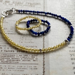 May include: A set of two bracelets, one with yellow beads and one with blue beads. The bracelets are on a white surface with text.