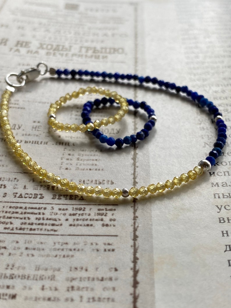 May include: A set of two bracelets, one with yellow beads and one with blue beads. The bracelets are on a white surface with text.