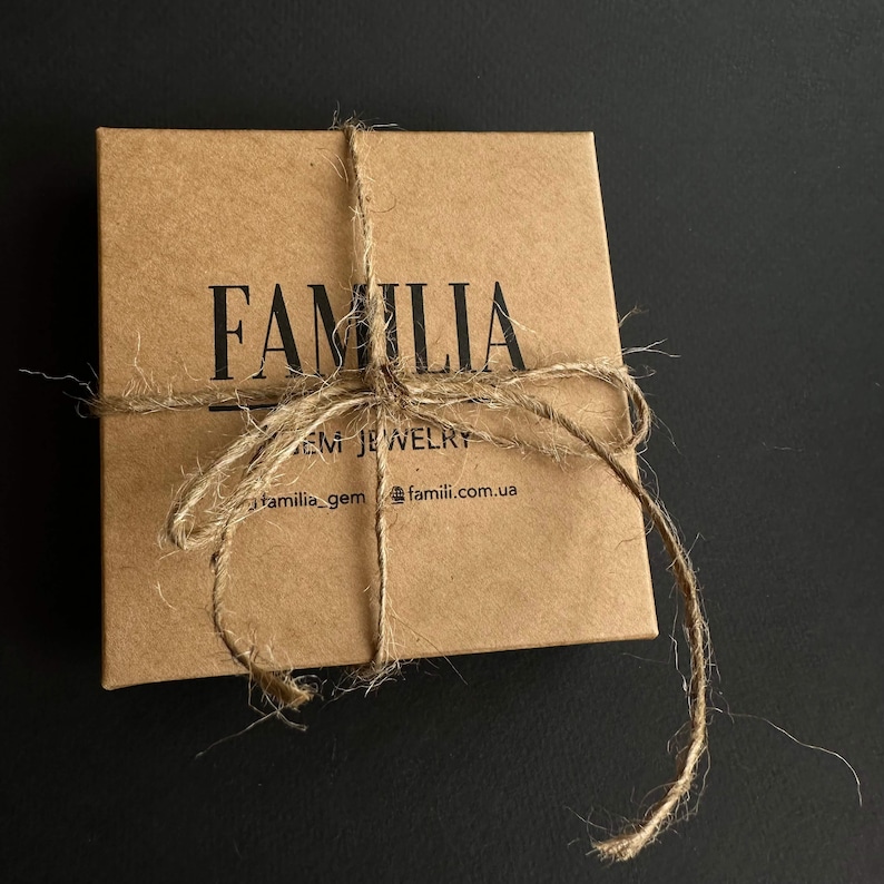 Może przedstawiać: Brązowe pudełko kartonowe z nadrukiem słowa "FAMILIA" w kolorze czarnym. Pudełko jest związane sznurkiem i ma nadrukowany tekst "GEM JEWELRY" oraz "familia_gem @famili.com.ua" na przodzie.