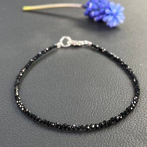 May include: A delicate black gemstone bracelet with a silver clasp. The bracelet is made of small, faceted black gemstones and is strung on a silver chain.