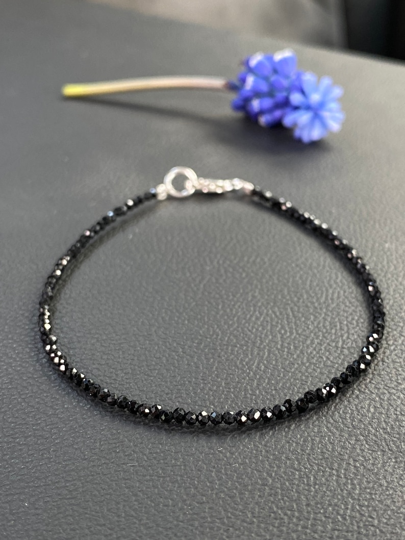 May include: A delicate black gemstone bracelet with a silver clasp. The bracelet is made of small, faceted black gemstones and is strung on a silver chain.