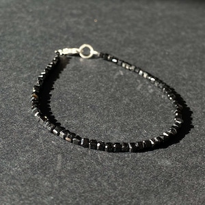 May include: A black beaded bracelet with a silver clasp. The beads are square shaped and have a matte finish.