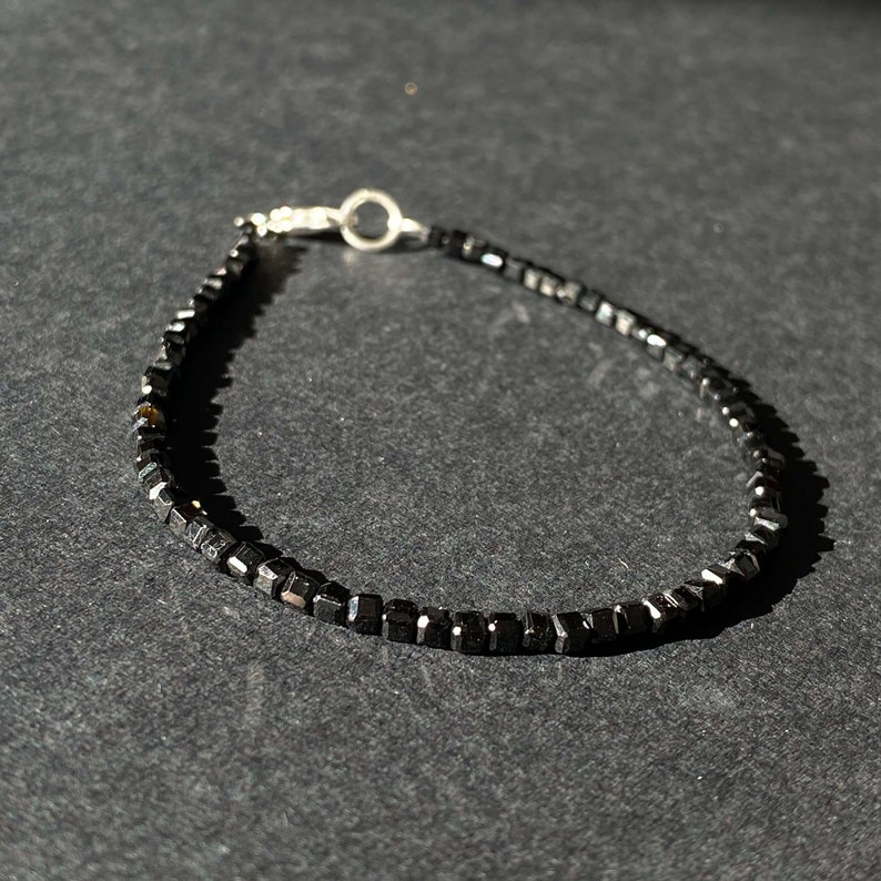 May include: A black beaded bracelet with a silver clasp. The beads are square shaped and have a matte finish.