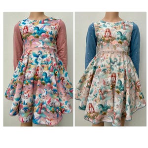 Peut inclure: Deux robes à manches longues avec un imprimé de licorne et de fée. Une robe a un corsage rose et des manches bleues, l'autre a un corsage bleu et des manches roses.