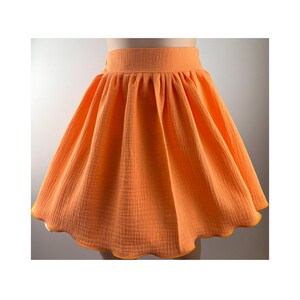 Könnte beinhalten: Ein leuchtend orangefarbener Rock mit einem gewellten Saum. Der Rock ist aus einem weichen, strukturierten Stoff.