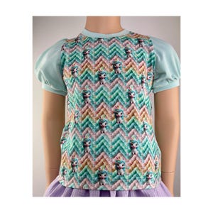 Peut inclure: Un t-shirt bleu clair à manches bouffantes et un motif chevron coloré avec des licornes de dessin animé. Le t-shirt a un col rond et est fait d'un tissu doux et confortable.