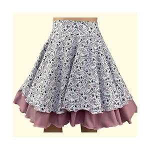 以下が含まれることがあります： 猫の顔のプリントが施された白いスカートと、ピンクのフリルのある裾です。