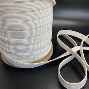 May include: A spool of white elastic cord, wound tightly, with a length of the cord extending from the spool.