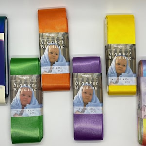 May include: Assortment of Wrights brand satin and fancy blanket binding in various colors, including green, orange, yellow, purple, and a multi-colored ombre. Each roll is 4 1/4 yards (4.35 meters) long.