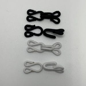 May include: Four black and white elastic loop and hook closures. The closures are used for clothing, bags, or other items.