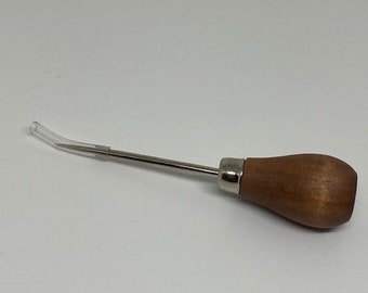 May include: A wooden handled tool with a metal needle and a clear plastic tip. The tool is used for leather crafting.