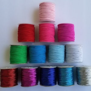 May include: Assortment of 12 spools of colorful elastic cord, in various colors including pink, red, green, blue, white, silver, and gold. The spools are arranged in a pyramid shape.