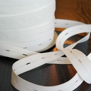 May include: White elastic with evenly spaced buttonholes. The elastic is rolled up on a spool.