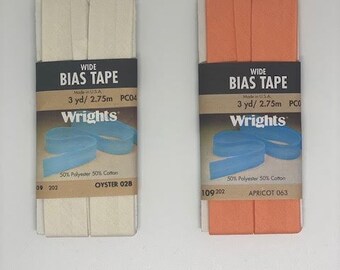 May include: Two rolls of wide bias tape, one in oyster white and one in apricot orange. Each roll is 3 yards long and made of 50% polyester and 50% cotton. The packaging includes the brand name "Wrights" and the color name.