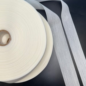 May include: A roll of white fabric tape with a white fabric tape strip lying next to it. The tape is likely used for sewing or crafts.