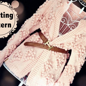 May include: A pink knitted cardigan with a heart-shaped stitch pattern and a brown belt. The cardigan has a V-neck and long sleeves.
