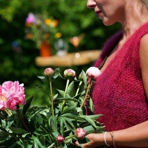 Könnte beinhalten: Eine Frau trägt eine rosa, flauschige, ärmellose Weste und hält einen Strauß rosa und weißer Pfingstrosen.