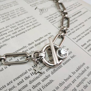 May include: A silver chain necklace with a silver toggle clasp and a star charm. The clasp has a clear crystal stone.