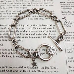 May include: A silver chain bracelet with a silver toggle clasp and a star charm. The bracelet has a clear crystal charm and is on a white background with text about macrame knots.