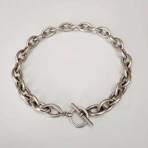 Puede incluir: Un collar de cadena de plata con cierre de palanca. La cadena est&aacute; hecha de eslabones gruesos de forma ovalada.