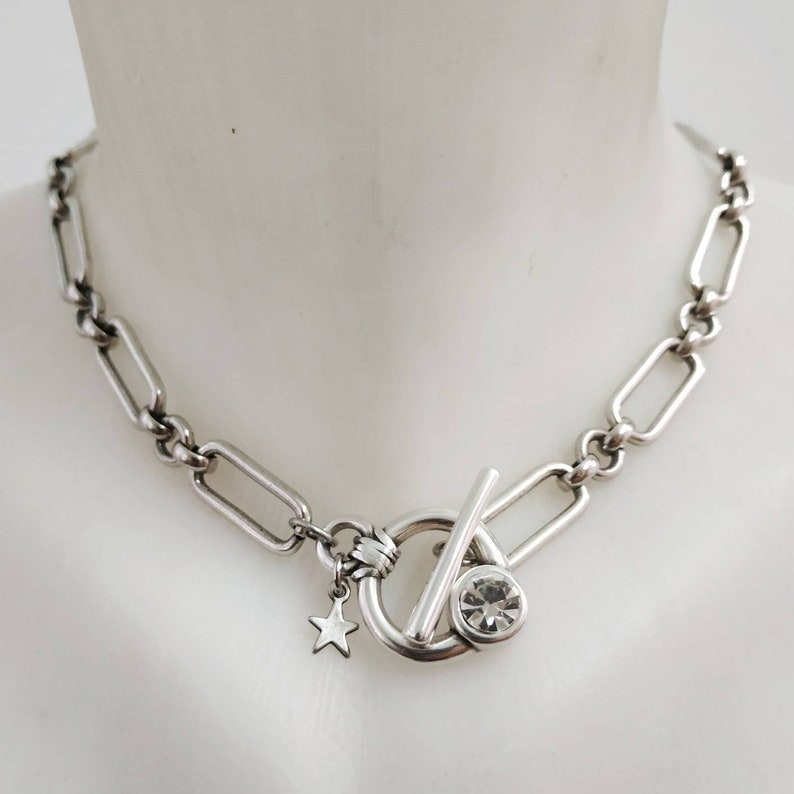 May include: A silver chain necklace with a toggle clasp featuring a clear rhinestone. A small star charm hangs from the clasp.