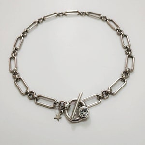 May include: A silver chain necklace with a toggle clasp featuring a clear rhinestone. A small star charm hangs from the clasp.