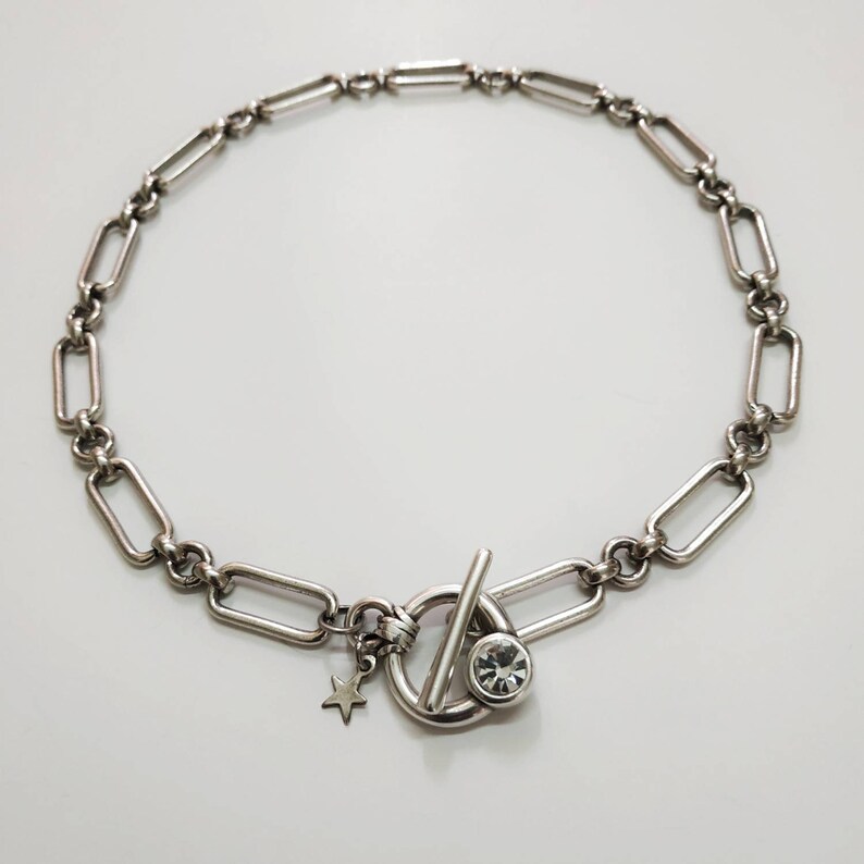 May include: A silver chain necklace with a toggle clasp featuring a clear rhinestone. A small star charm hangs from the clasp.