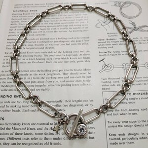 May include: A silver chain necklace with a star charm, a toggle clasp, and a clear rhinestone. The necklace is on a white background with text about knotting techniques.